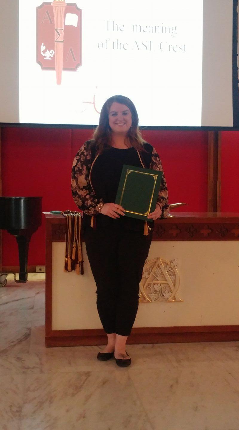 Alyssa stands on the altar of Norton Chapel holding her honor society induction certificate